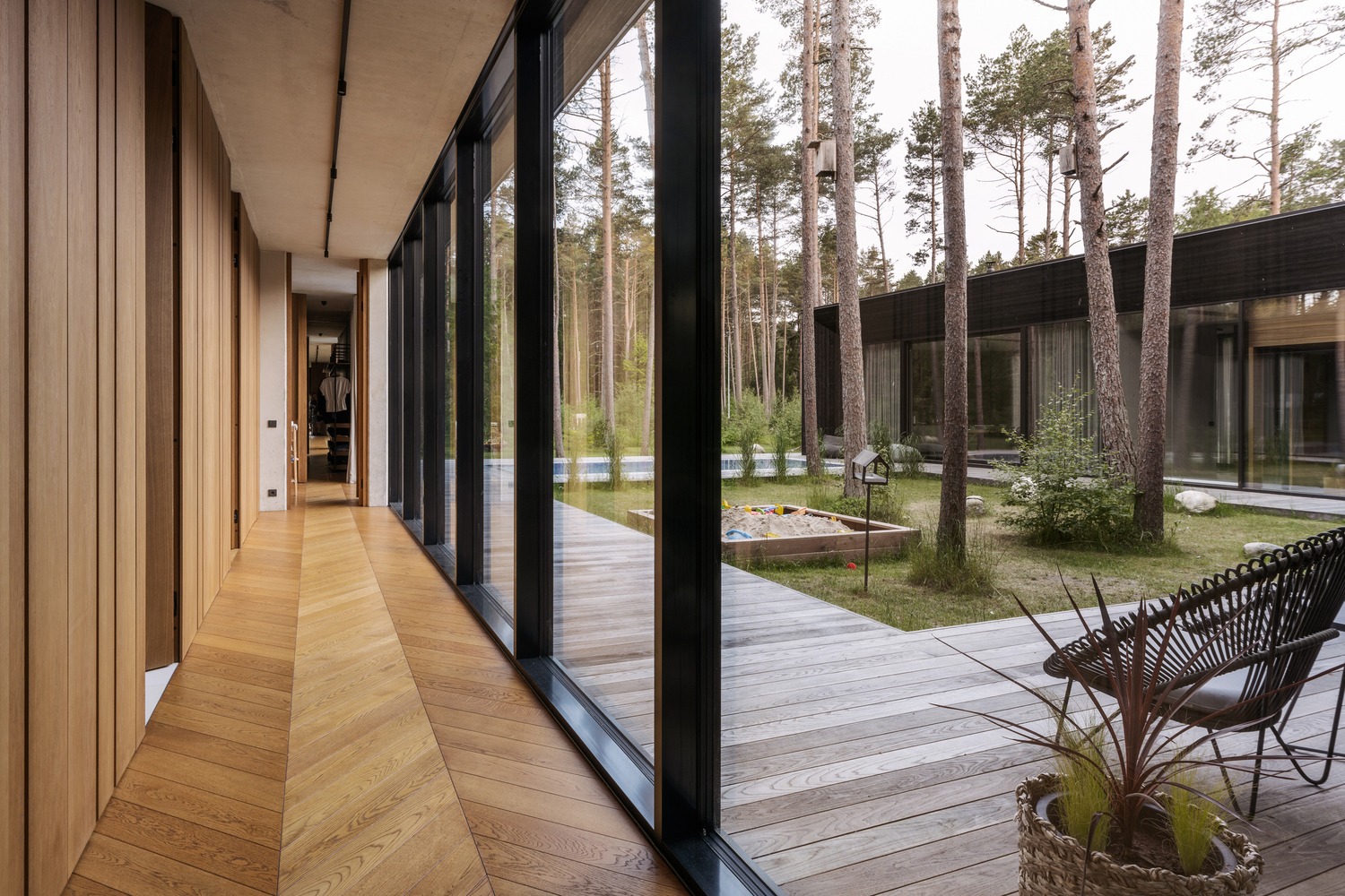 Nowoczesny, przestronny dom z dużymi oknami wychodzącymi na drewniany taras, piaskownicę i zieleń. Parkiet w jodełkę, drewniane panele ścienne.