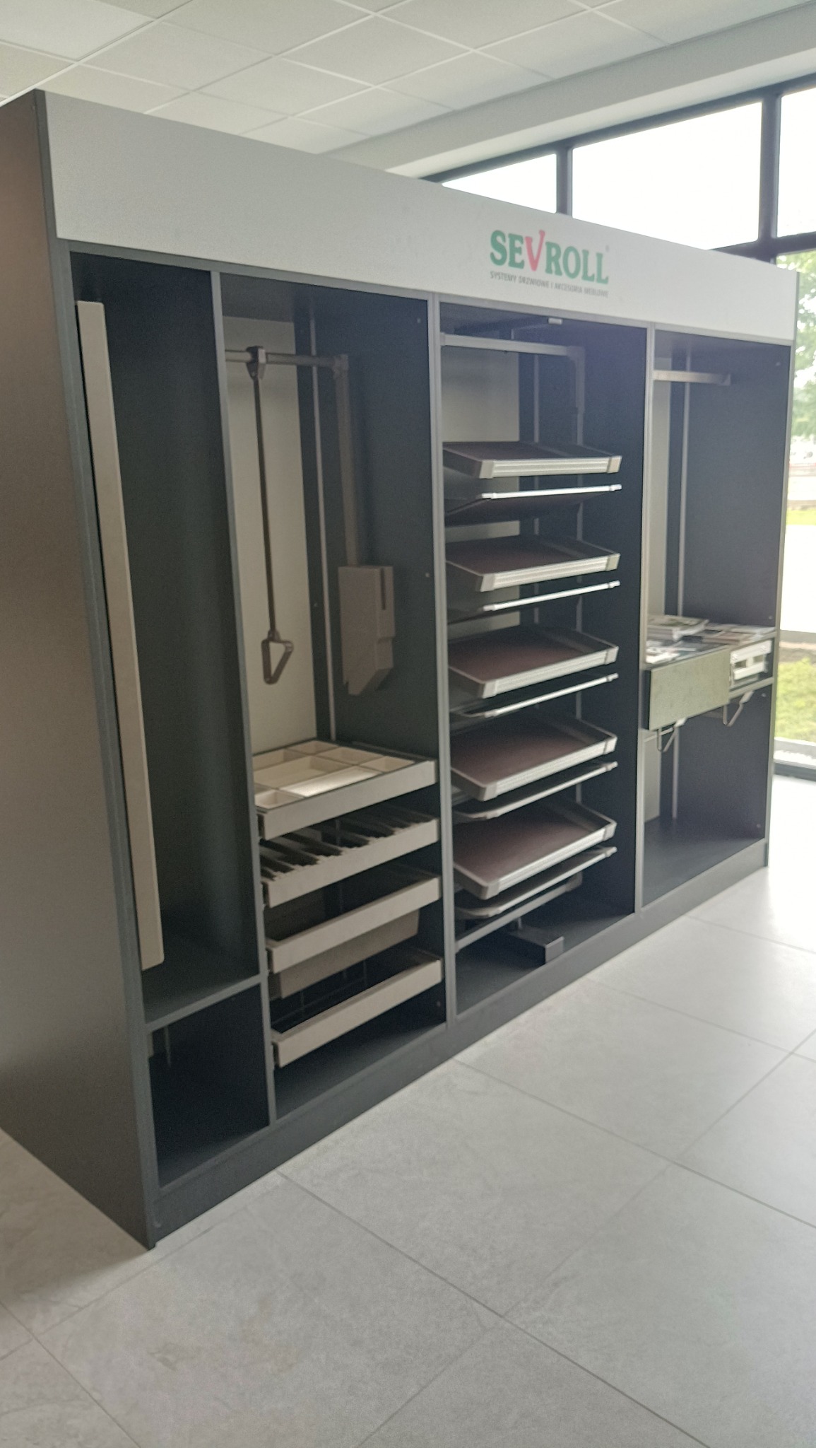 Szara szafa wnękowa z systemem półek i szuflad. Widoczne akcesoria i mechanizmy wewnętrzne. Prezentacja funkcjonalności i organizacji przestrzeni.