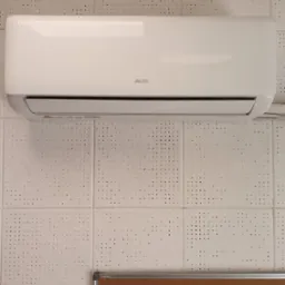 Biały klimatyzator marki AUX zamontowany na ścianie z panelami o perforowanej strukturze. Tablica informacyjna widoczna w dolnej części zdjęcia.