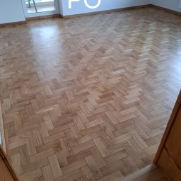 PRO-PODŁOGI - układanie , renowacja - Parkiet ułożony w jodełkę, widok po renowacji. Jasne drewno, naturalne oświetlenie, balkon w tle. Na ścianie napis 'PO' sugerujący efekt po usłudze.