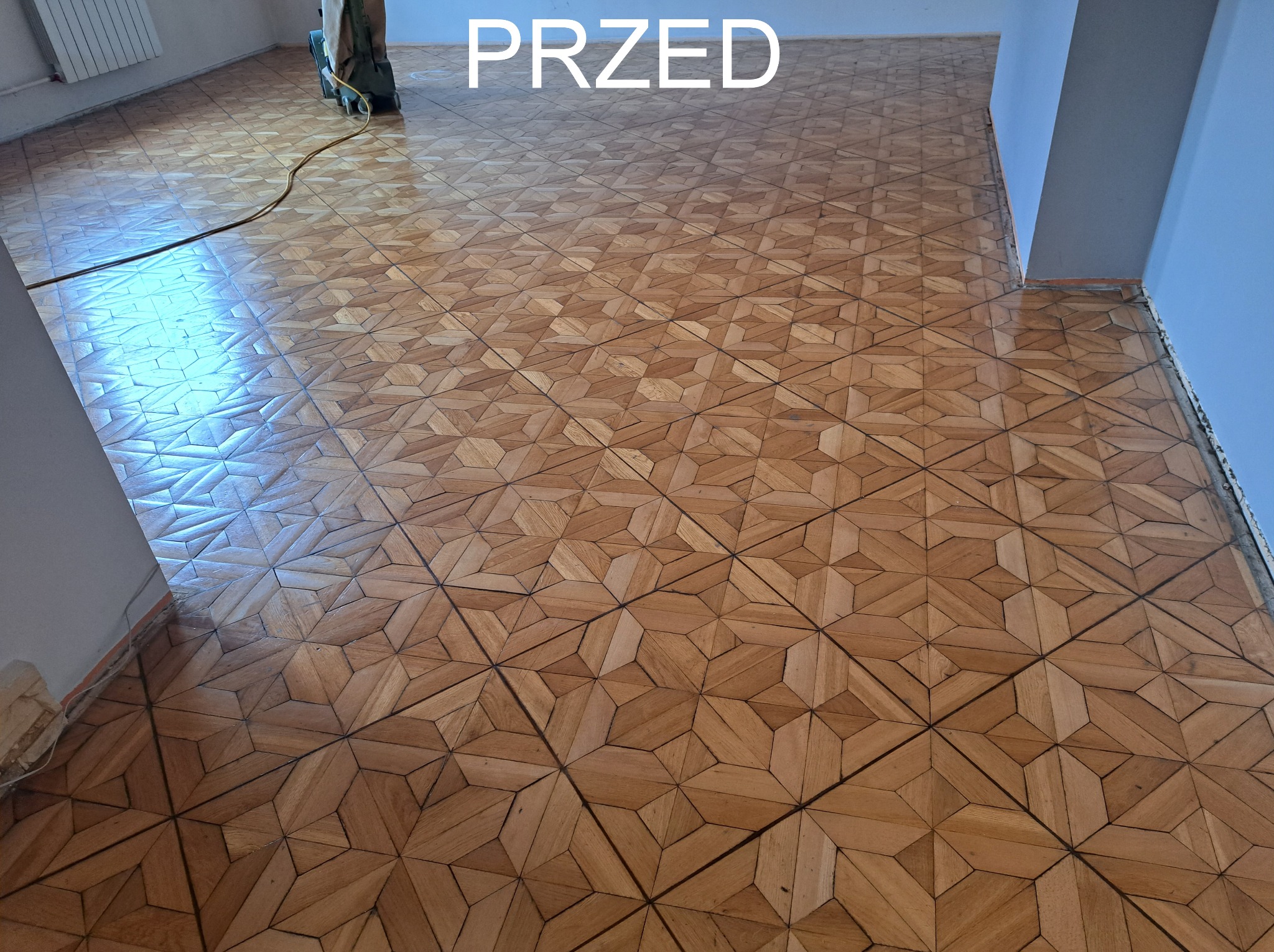 Parkiet mozaikowy 'przed' renowacją, widoczna maszyna do cyklinowania w tle, jasne drewno, wzór geometryczny, przygotowanie do odświeżenia podłogi.