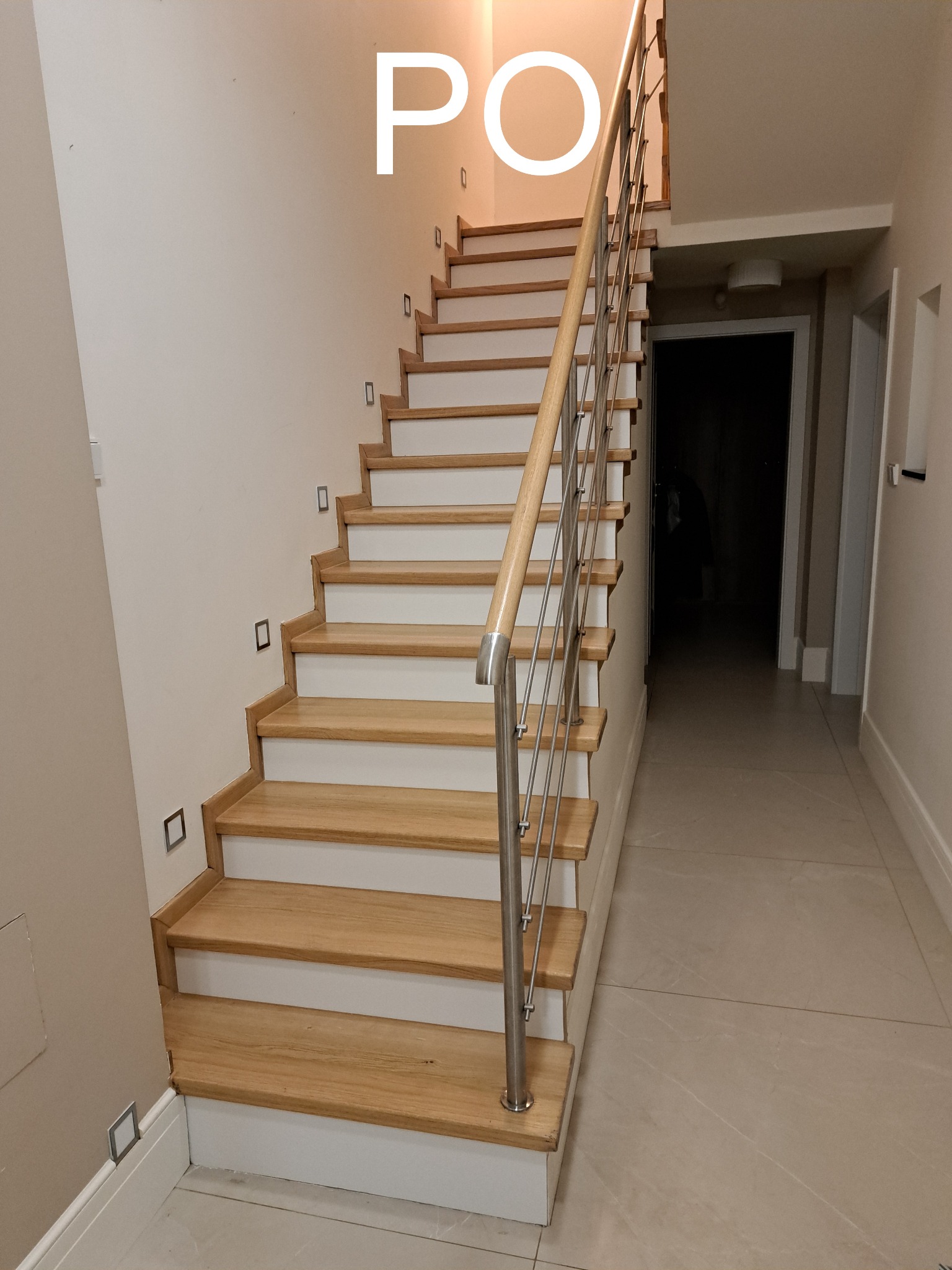 Odnowione schody drewniane z białymi podstopnicami i metalową balustradą, oświetlone punktowo, widok z dołu, po remoncie.