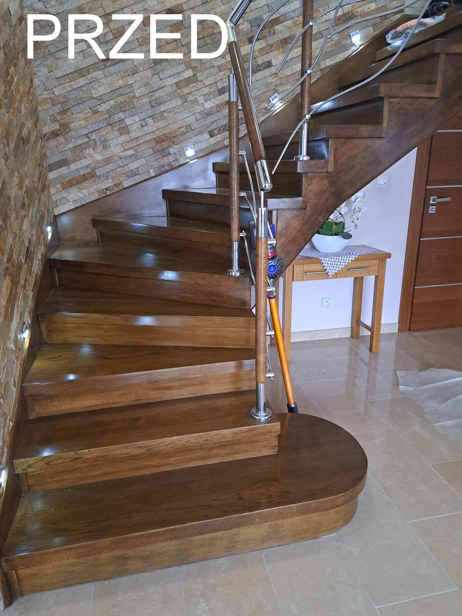 Drewniane schody z metalową balustradą w domu z kamienną ścianą, oświetleniem punktowym i tekstem 'PRZED' na górze zdjęcia. Widoczny odkurzacz.