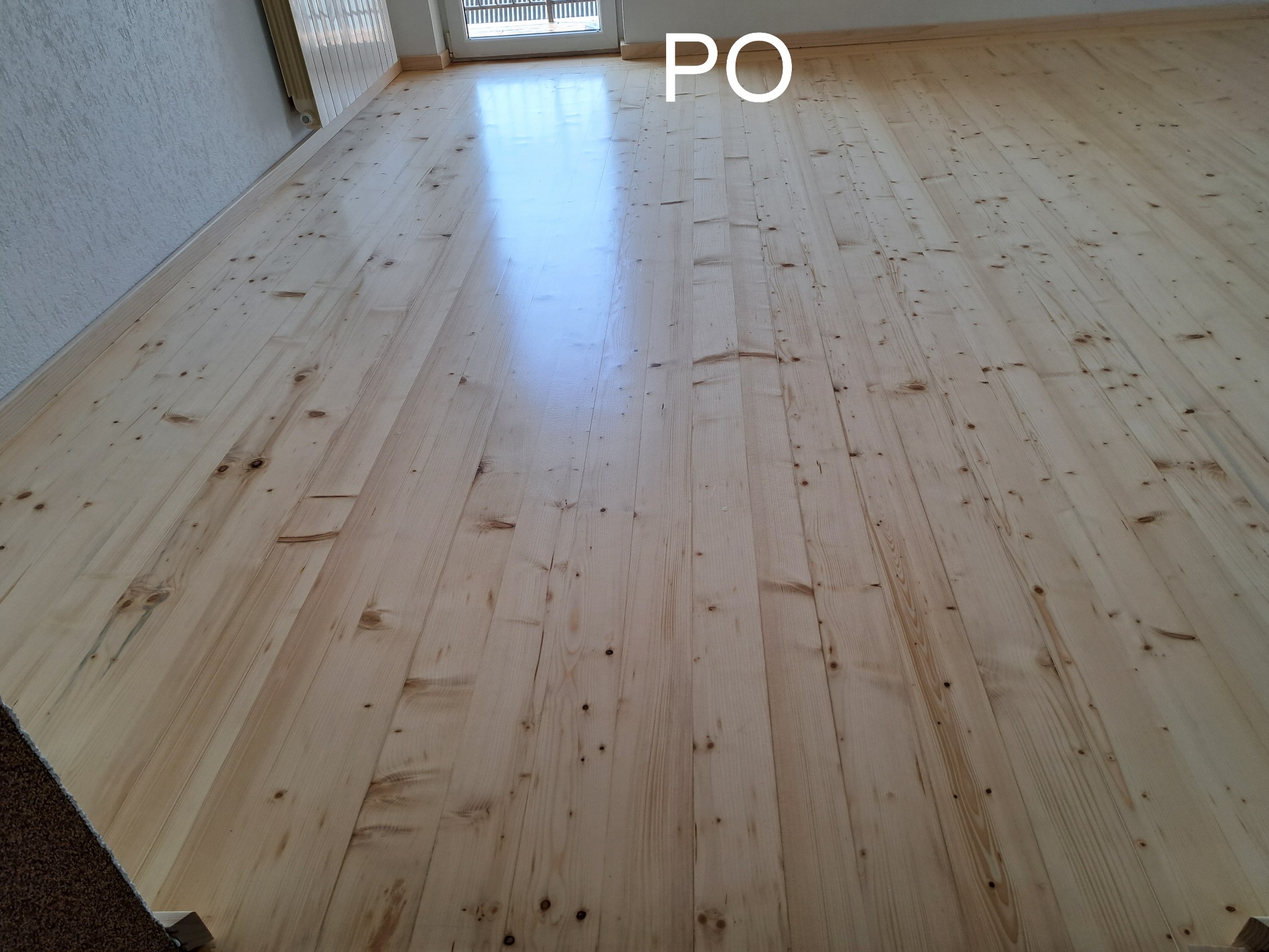 Jasne, odnowione deski podłogowe z widocznym rysunkiem drewna i połyskiem, oświetlone naturalnym światłem, ukazane w szerokim planie.