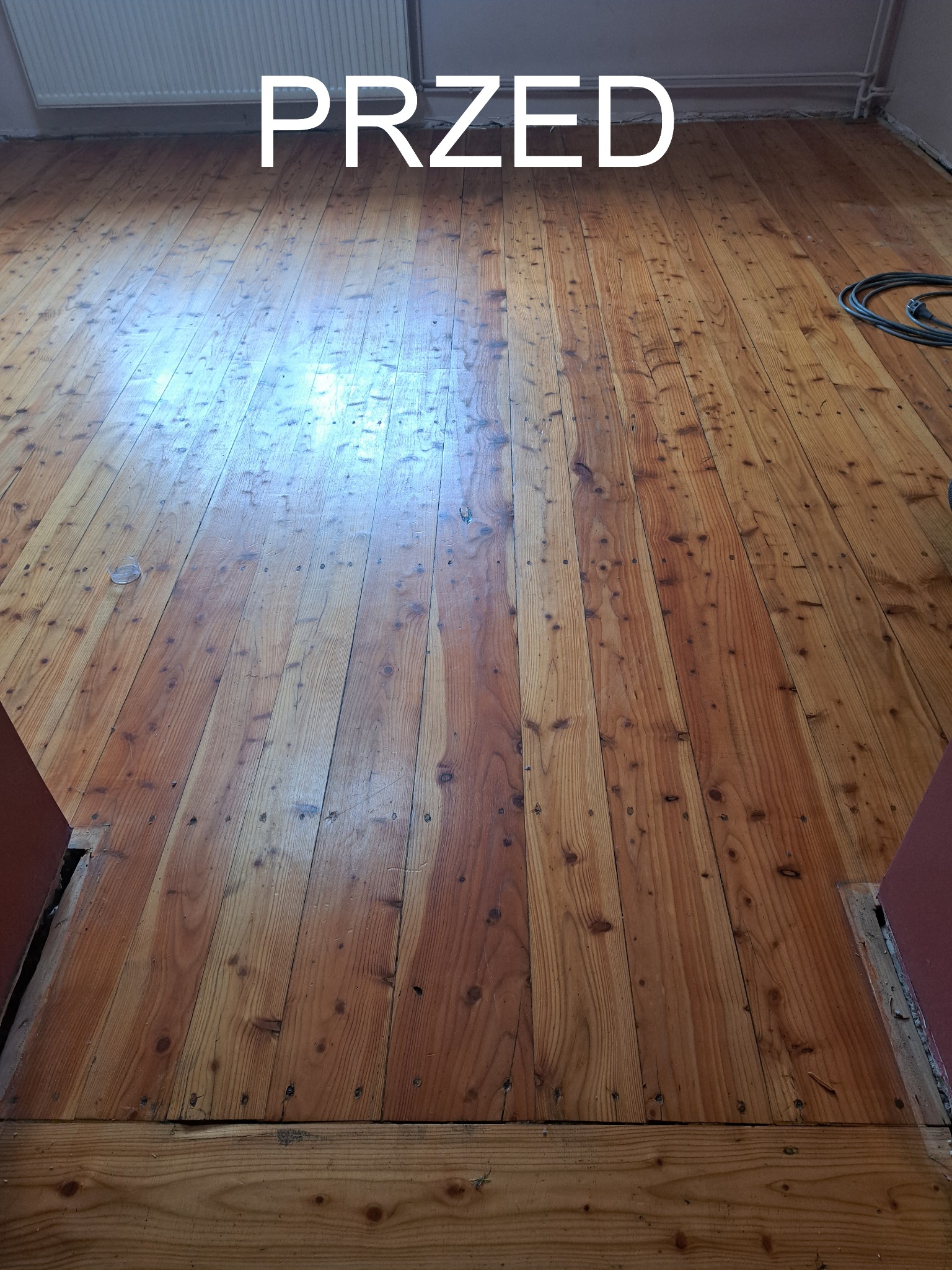 Drewniana podłoga przed renowacją. Widoczne stare deski z licznymi śladami użytkowania, rysami i ubytkami. Napis 'PRZED' sugeruje etap prac.