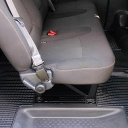 Mateusz Jachowski - Szare, tapicerowane siedzenie w samochodzie z pasami bezpieczeństwa i gumową wycieraczką podłogową. Widok z wnętrza pojazdu przez otwarte drzwi.