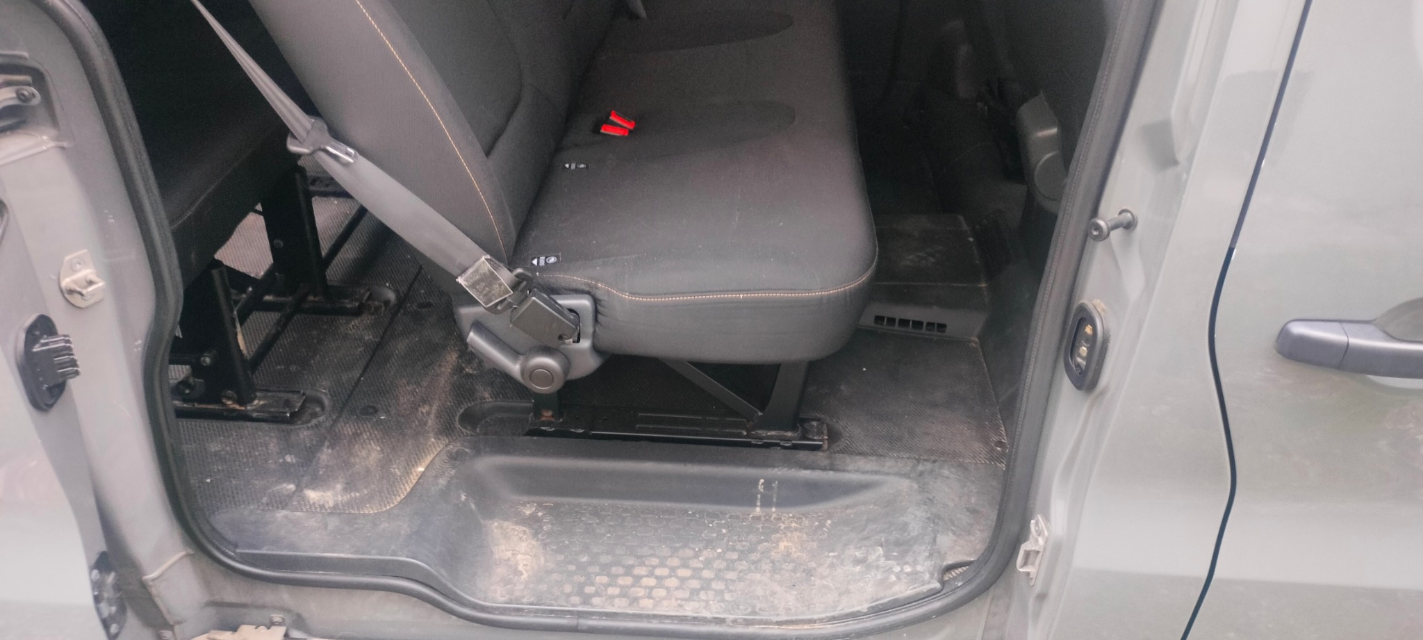 Wnętrze brudnego samochodu dostawczego z widocznym siedzeniem i podłogą wymagającą czyszczenia. Fotel z pasami bezpieczeństwa. Widok przez otwarte drzwi.