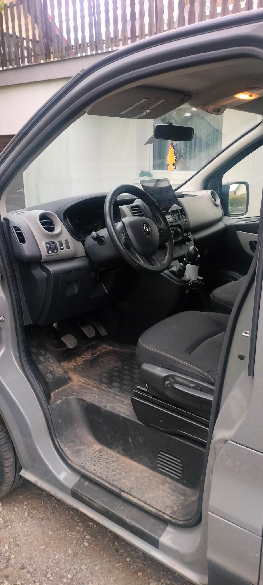 Wnętrze szarego samochodu dostawczego z otwartymi drzwiami. Widoczna deska rozdzielcza, kierownica, fotel kierowcy i bardzo zabrudzona podłoga.