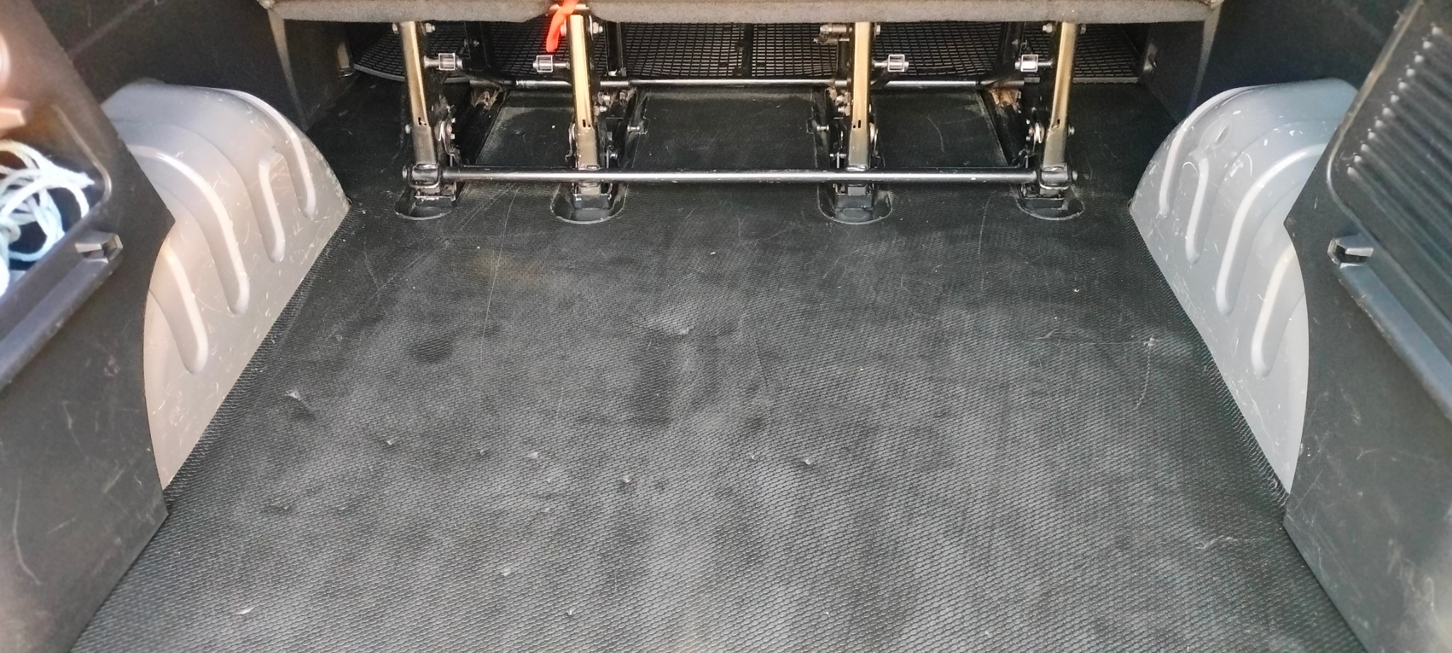 Wnętrze bagażnika samochodu dostawczego z zamontowanymi szynami do siedzeń, widok z góry na czarną, gumową podłogę. Widoczne ślady użytkowania.