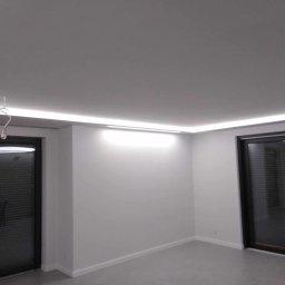 ALEX AG - Minimalistyczne wnętrze z białymi ścianami, szarą podłogą i subtelnym oświetleniem LED wzdłuż sufitu, podkreślającym nowoczesny charakter pomieszczenia.