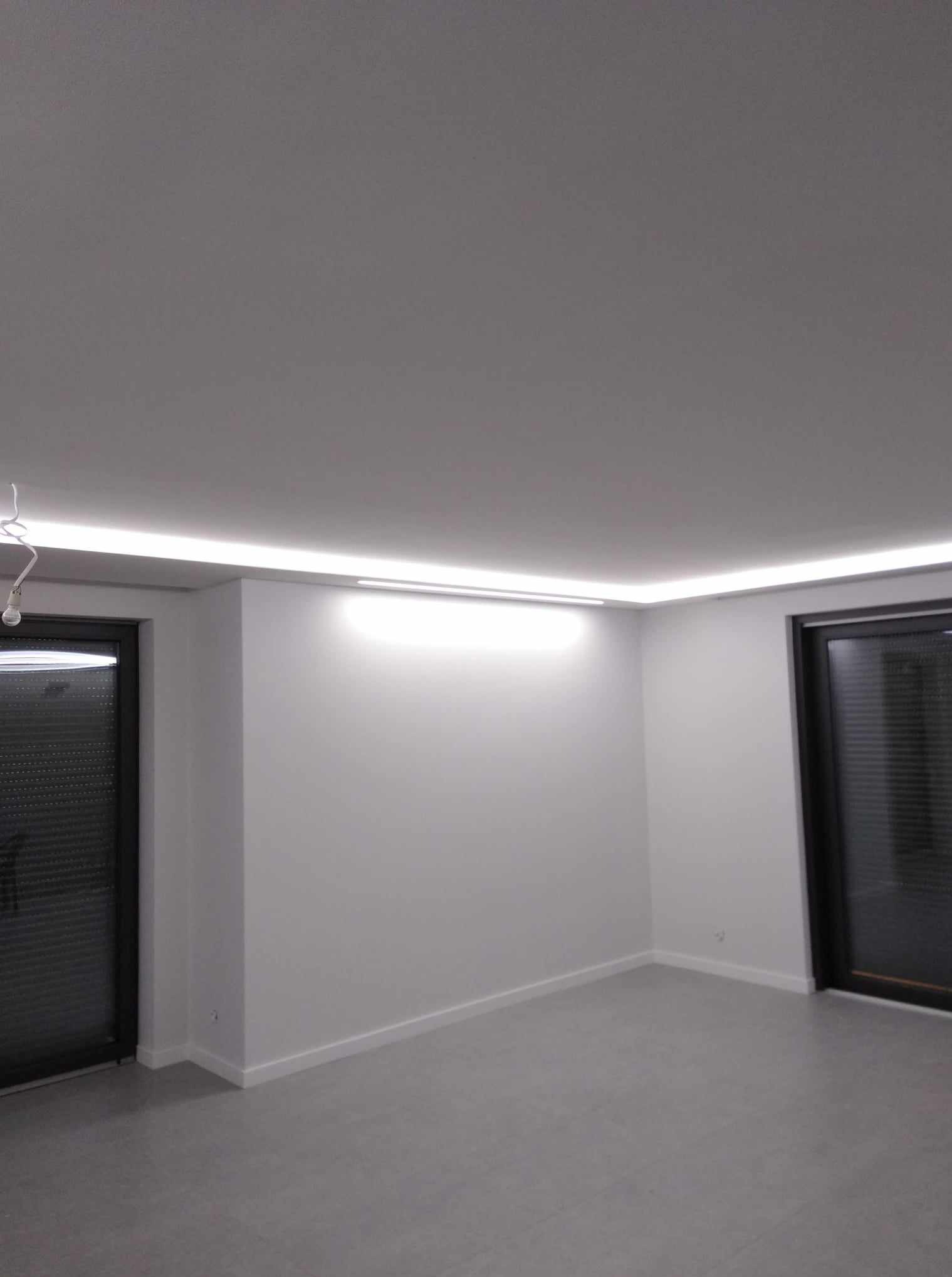 Minimalistyczne wnętrze z białymi ścianami, szarą podłogą i subtelnym oświetleniem LED wzdłuż sufitu, podkreślającym nowoczesny charakter pomieszczenia.