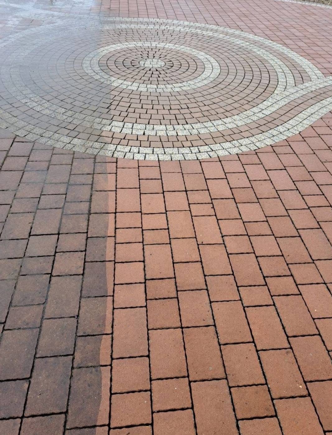 Efekt mycia kostki brukowej: różnica między czystą, mokrą częścią a brudną, suchą. Okrągły wzór z jaśniejszych kostek. Widok z góry, w kadrze cała kostka.