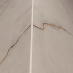 Detal narożnika wykończonego płytkami imitującymi marmur z fugą. Widoczny fragment kratki wentylacyjnej w górnej części.