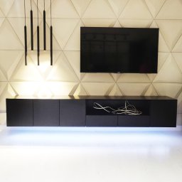 STOLARECZKA - Minimalistyczna, czarna szafka RTV wisząca pod telewizorem, z podświetleniem LED. Na ścianie trójwymiarowa faktura i designerskie lampy wiszące.