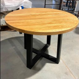 STOLARECZKA - Okrągły stół z blatem z jasnego drewna i czarną, metalową podstawą w kształcie litery X, widoczny w warsztacie stolarskim.