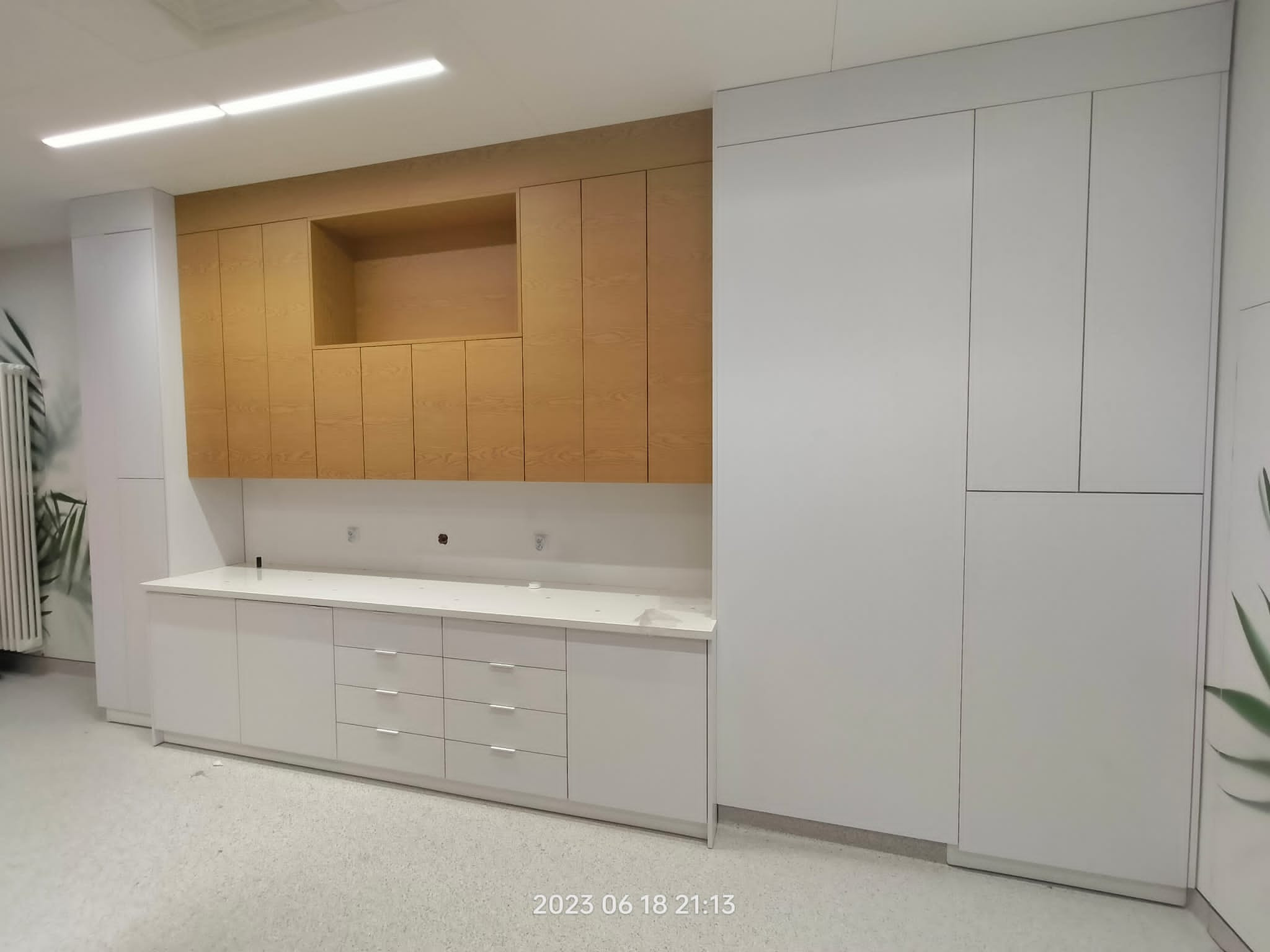 Nowoczesna zabudowa kuchenna z białymi szafkami dolnymi i drewnianymi górnymi, z otwartą półką. Minimalistyczny design, jasne wnętrze.