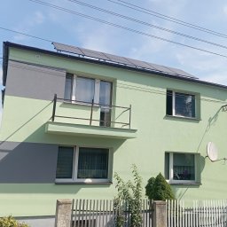 ON BUD Michał Zejer - Dom z balkonem po malowaniu elewacji na jasnozielono i szaro, z panelami słonecznymi na dachu. Widoczna antena satelitarna i ogrodzenie.