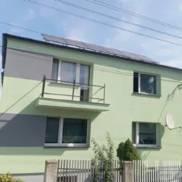 Dom z balkonem po malowaniu elewacji na jasnozielono i szaro, z panelami słonecznymi na dachu. Widoczna antena satelitarna i ogrodzenie.