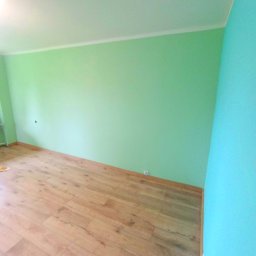 ON BUD Michał Zejer - Pomieszczenie po odświeżeniu: ściany pomalowane na zielono i błękitno, drewniana podłoga. Widok na odnowione wnętrze z perspektywy podłogi.