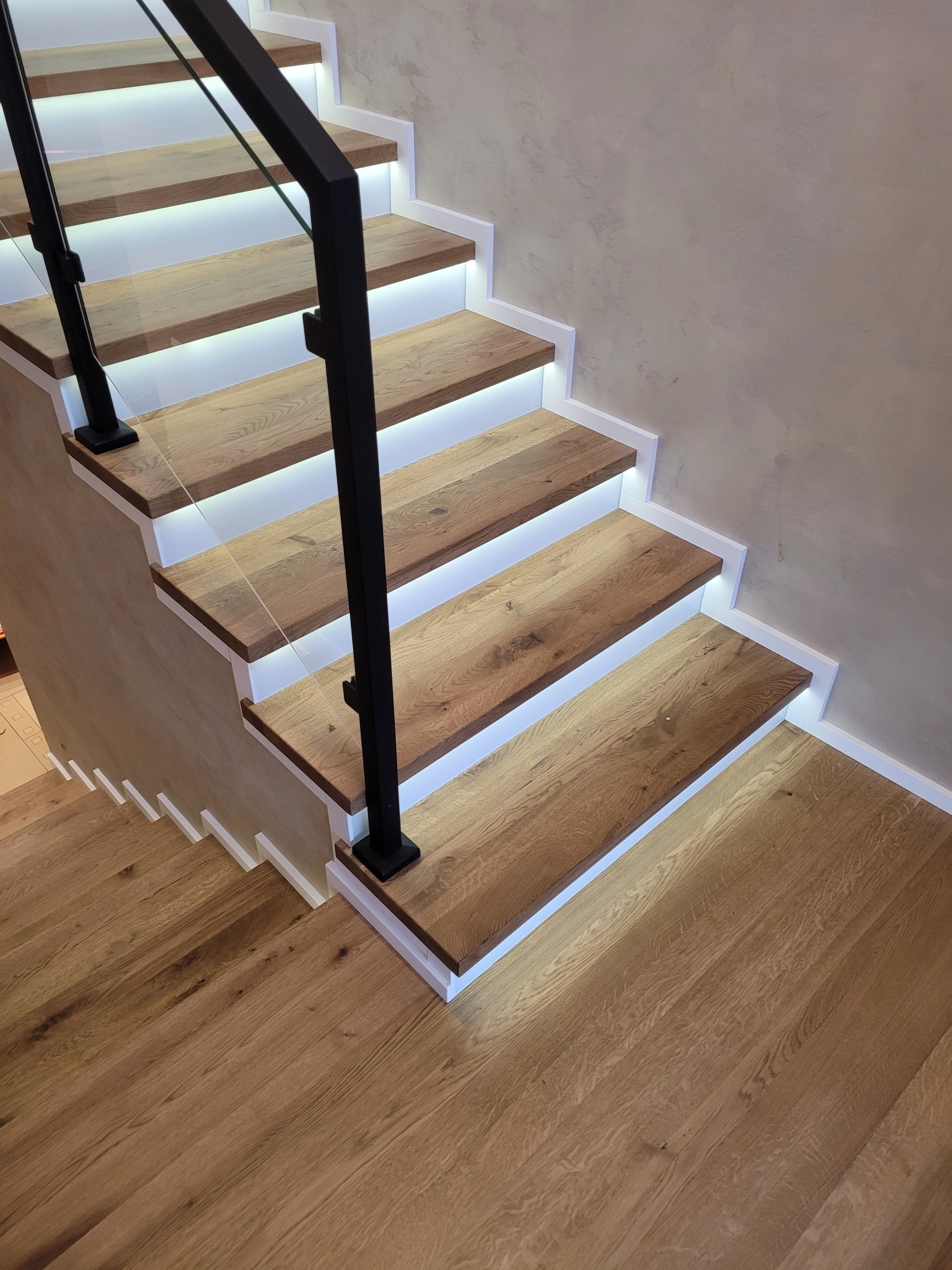 Nowoczesne schody drewniane z podświetleniem LED i szklaną balustradą, widok z góry.