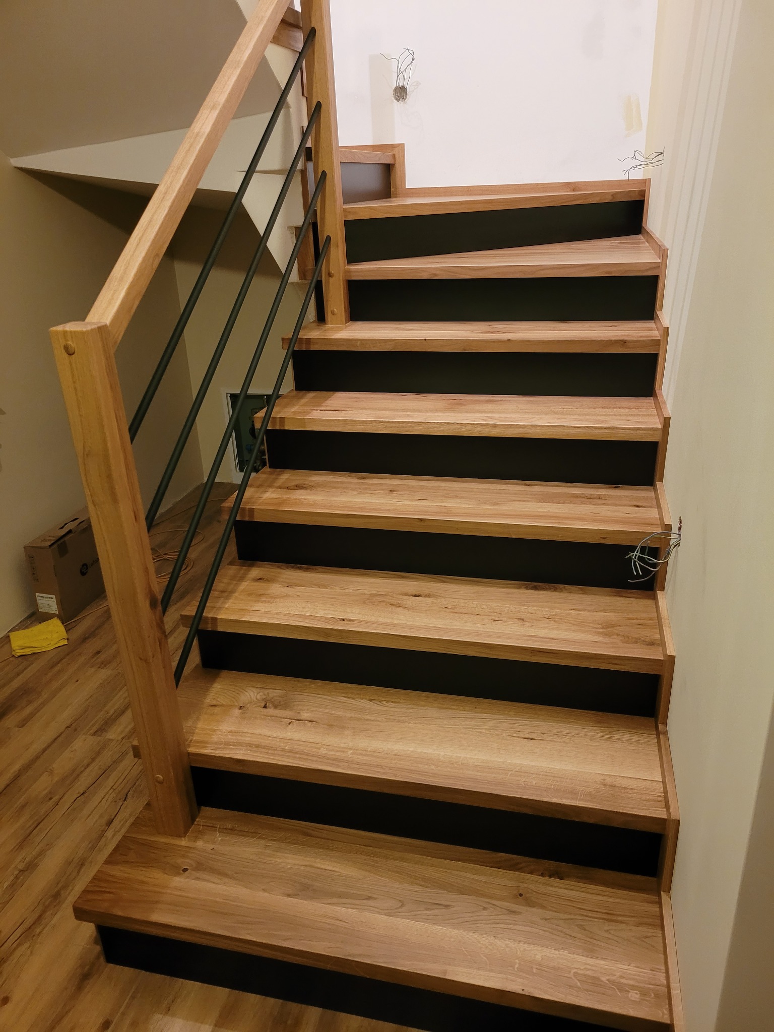 Nowoczesne schody z drewnianymi stopniami i czarnymi podstopnicami, z minimalistyczną balustradą z drewnianymi słupkami i czarnymi prętami.