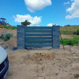 Montaż nowoczesnej, grafitowej bramy wjazdowej z pustaków betonowych. W tle widoczny sprzęt budowlany i błękitne niebo.