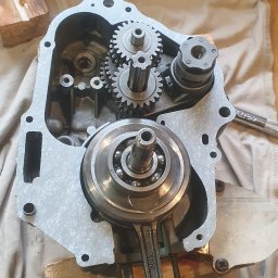 Mateusz Profus - Silnik motocykla w trakcie naprawy: widoczny wał korbowy, skrzynia biegów. Młotek w tle sugeruje warsztatowy charakter. Detal mechaniczny, naprawa, serwis.