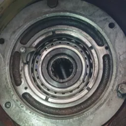 Wnętrze piasty koła z widocznymi łożyskami i elementami mocującymi. Detal mechanizmu z bliska, ukazujący zużycie i smar.