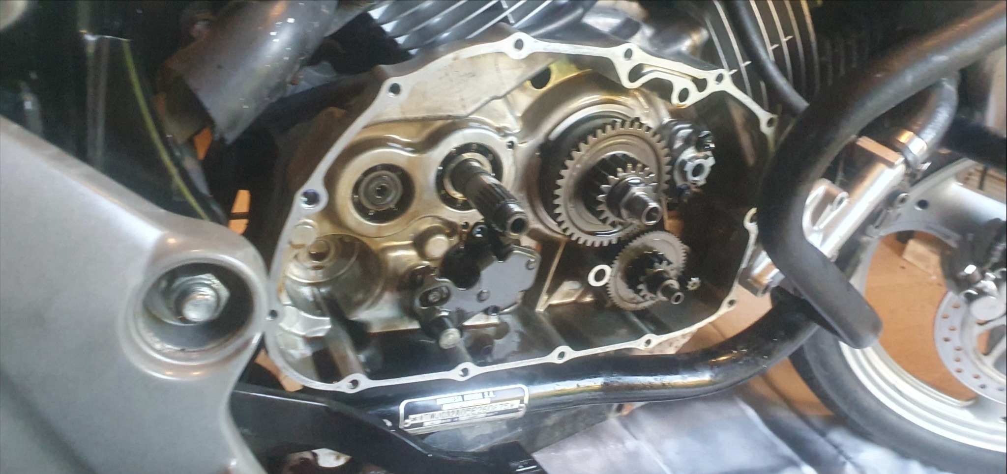 Otwarta obudowa silnika motocykla z widocznymi przekładniami i elementami mechanicznymi, ukazująca etap naprawy lub konserwacji.