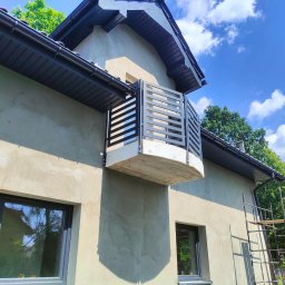 TECH-WELD - Szara, metalowa balustrada balkonowa z poziomymi szczebelkami w Będzinie. Widok z dołu na tle błękitnego nieba z chmurami i fragmentu elewacji domu.