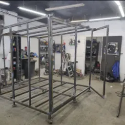 Stalowa konstrukcja szkieletowa w hali warsztatowej, spawana z profili kwadratowych, z widocznymi śladami spawania i narzędziami w tle. Etap budowy.