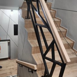 TECH-WELD - Nowoczesne schody z czarną, geometryczną balustradą i jasną drewnianą poręczą, widok z dołu, podkreślający designerski charakter konstrukcji i wykończenie wnętrza.