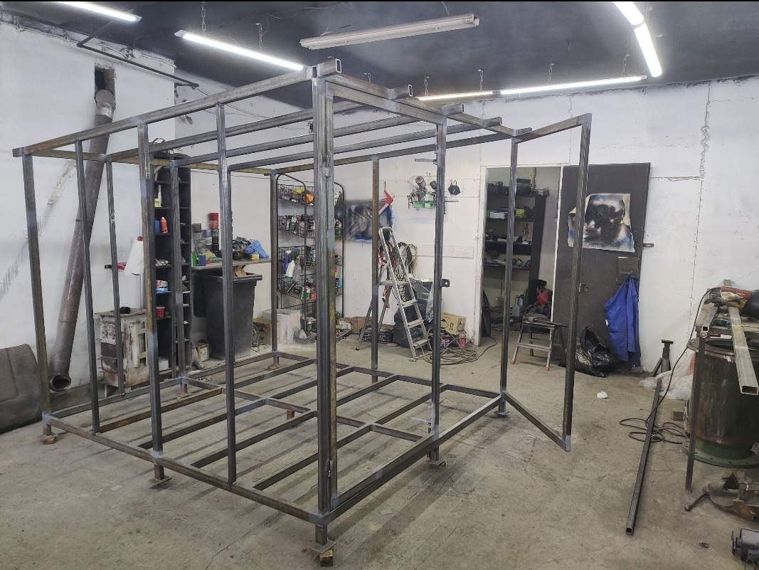 Stalowa konstrukcja szkieletowa w hali warsztatowej, spawana z profili kwadratowych, z widocznymi śladami spawania i narzędziami w tle. Etap budowy.