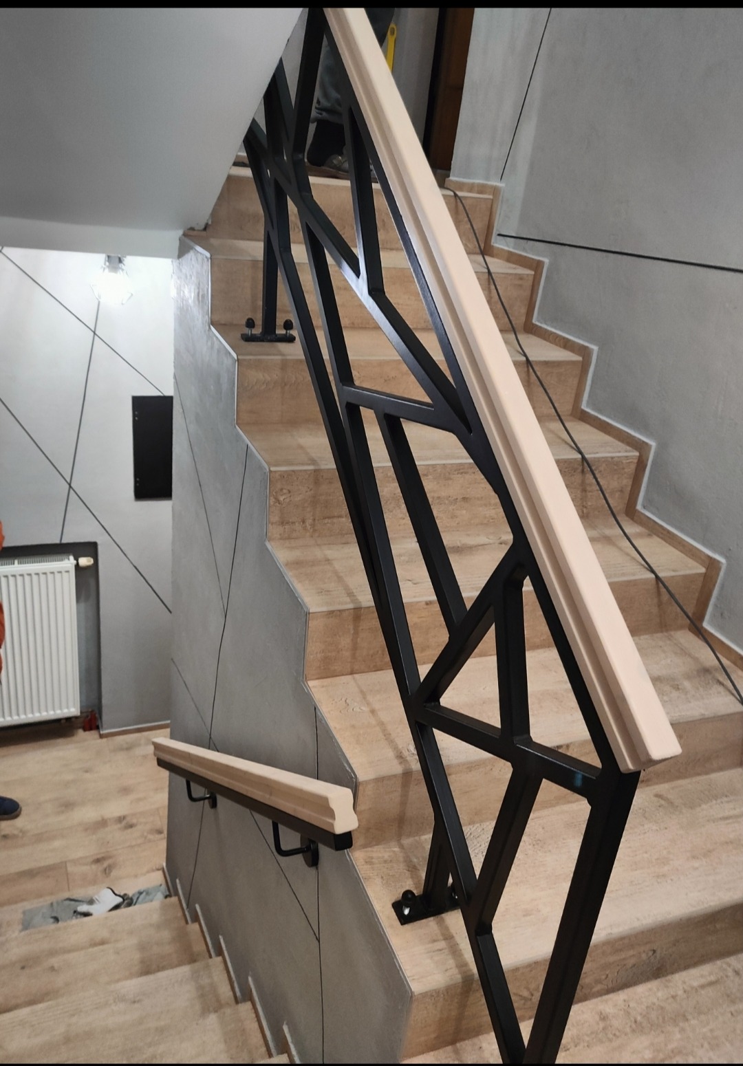 Nowoczesne schody z czarną, geometryczną balustradą i jasną drewnianą poręczą, widok z dołu, podkreślający designerski charakter konstrukcji i wykończenie wnętrza.