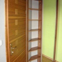 Red - Drewniana szafa wnękowa z przesuwnymi drzwiami lustrzanymi i półkami narożnymi, dopasowana do koloru drzwi wejściowych, na tle zielonej ściany.