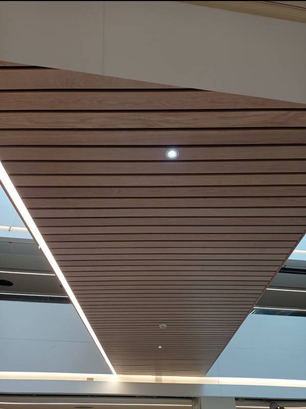 Drewniany sufit lamelowy z oświetleniem LED, widok z dołu. Geometryczny układ paneli tworzy nowoczesny design. Widoczne punkty świetlne.