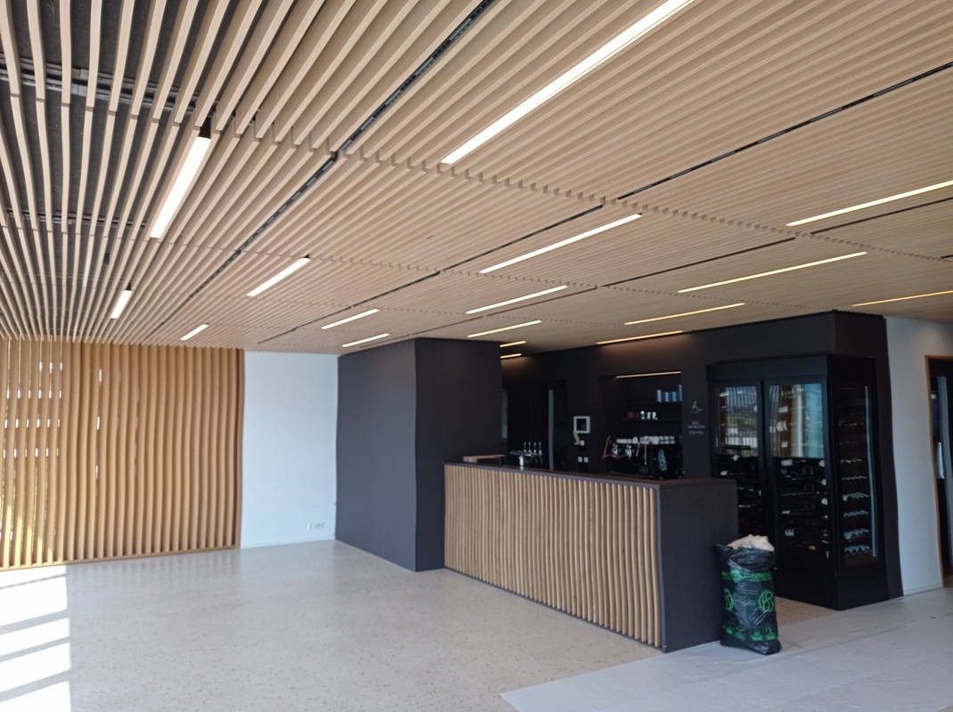 Nowoczesne wnętrze komercyjne z drewnianą zabudową sufitu i ścian, minimalistyczny bar z okładziną z pionowych listew i czarnymi elementami wyposażenia.