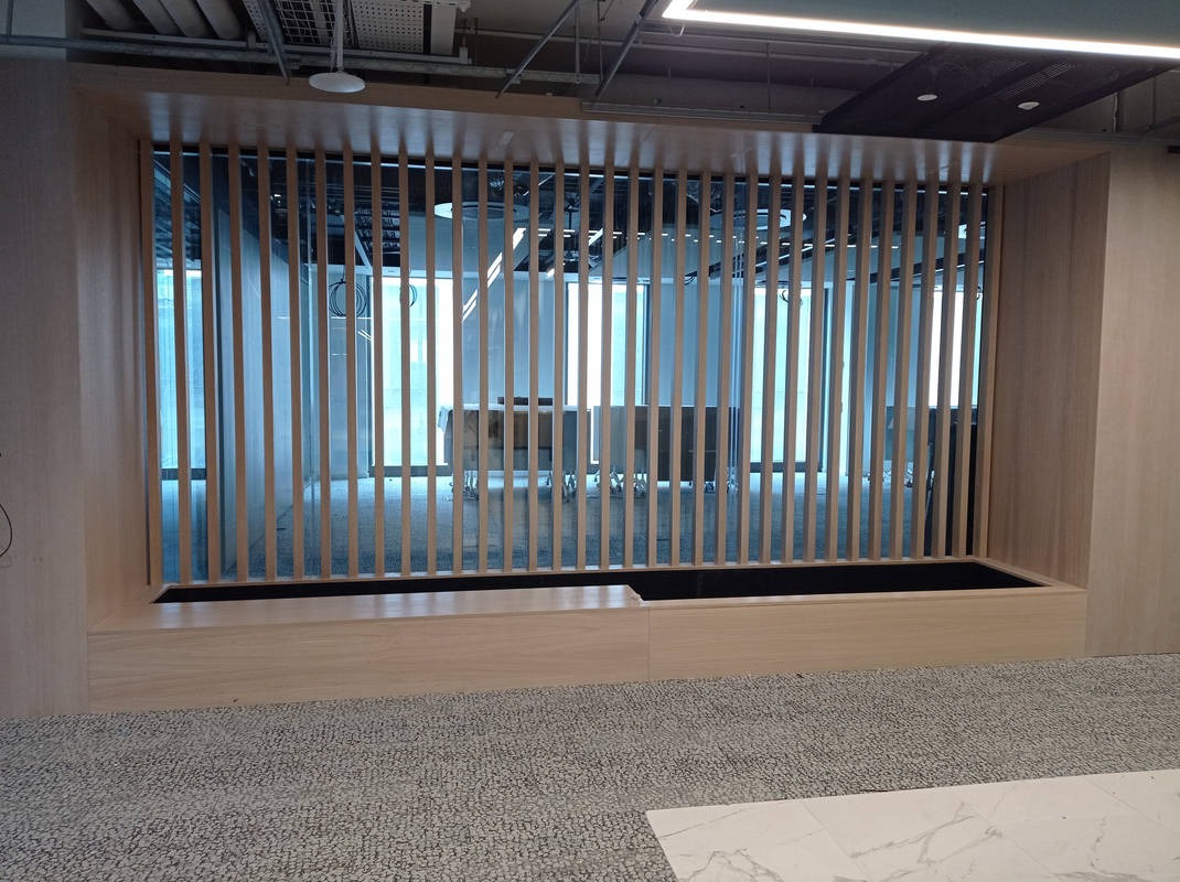 Nowoczesna drewniana ścianka działowa z pionowych listew w biurze. Widok na przestrzeń biurową z dużymi oknami. Element aranżacji wnętrza biurowego.