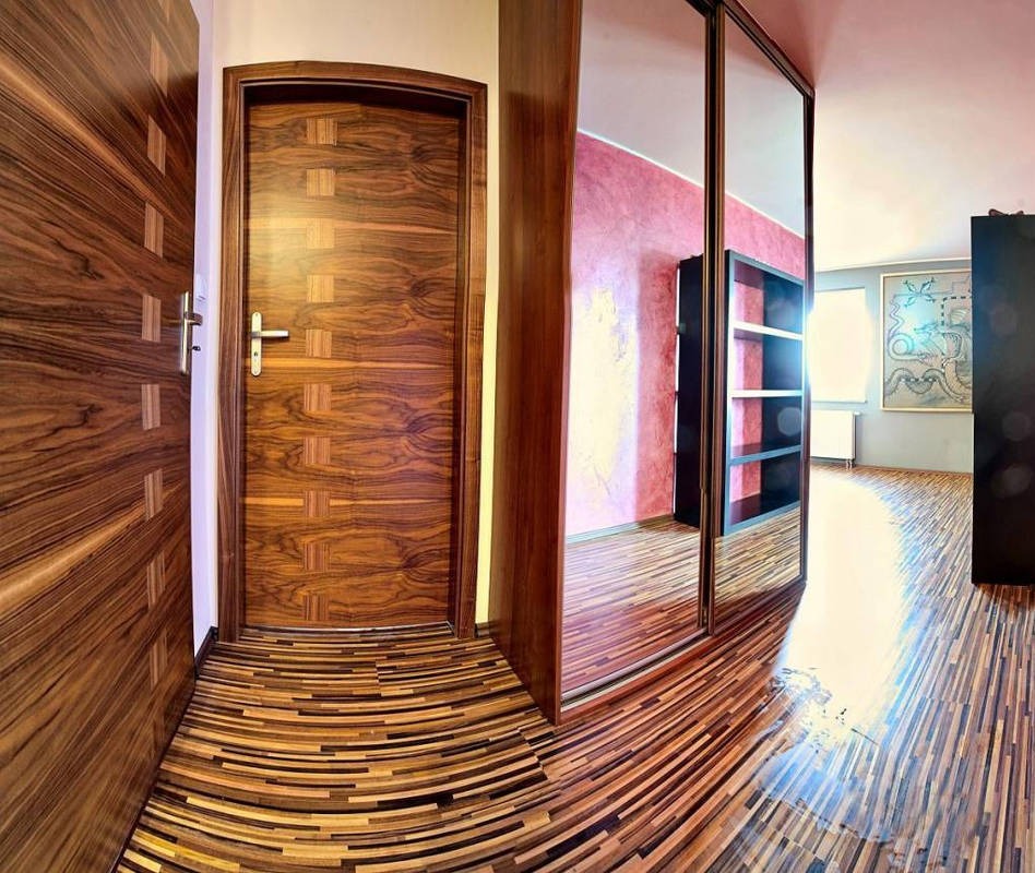 Wnętrze z drewnianą podłogą w łuki, dopasowanymi drzwiami i szafą z lustrzanymi drzwiami przesuwnymi. Widoczna ściana w odcieniach czerwieni i regał.