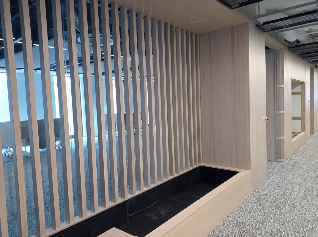 Nowoczesna drewniana ścianka działowa z pionowych listew, zintegrowana z donicą, w jasnym biurze z widocznymi elementami instalacji pod sufitem.