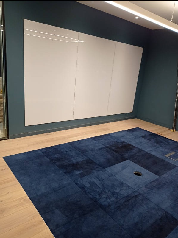 Nowoczesne biuro z ciemnoniebieskim dywanem w geometryczne wzory i białą ścianą z paneli, oświetlone światłem LED. Minimalistyczny design.