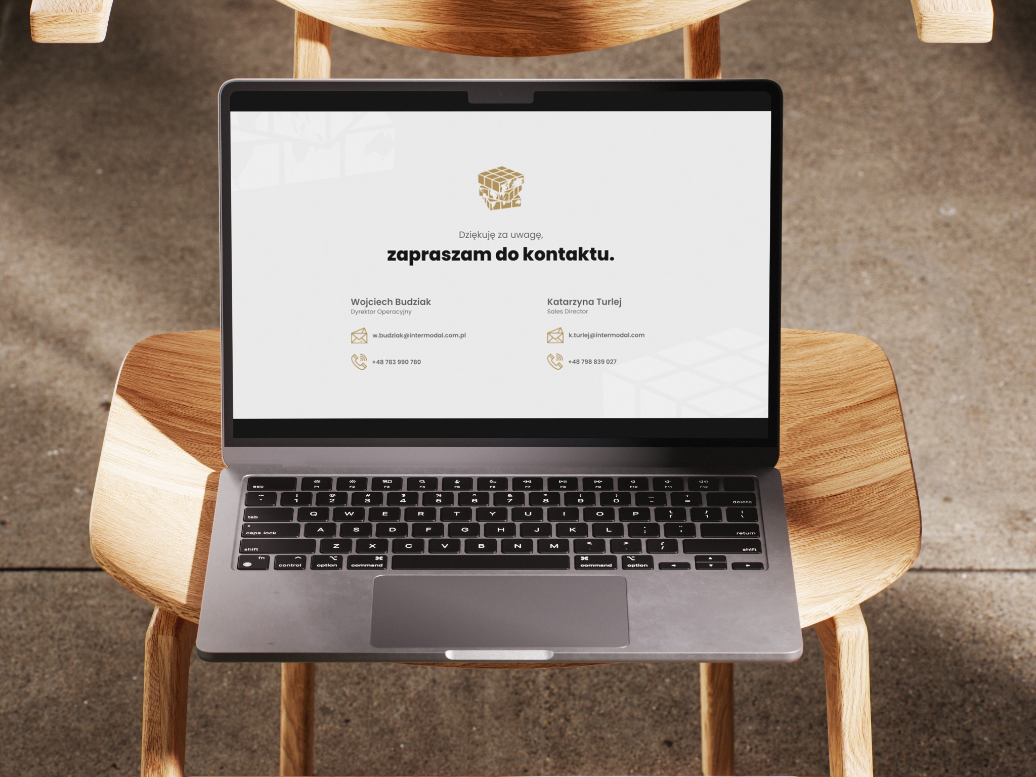 Laptop na krześle prezentuje stronę kontaktową z logo firmy, imionami i danymi kontaktowymi Wojciecha Budziaka i Katarzyny Turlej. Stonowana kolorystyka.