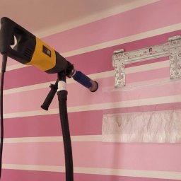 NEVCO Aleksander Kristof - Wiercenie otworu w różowej ścianie w paski pod montaż klimatyzacji. Uchwyt montażowy na ścianie, worek na pył. Wiertarka z odsysaniem pyłu.