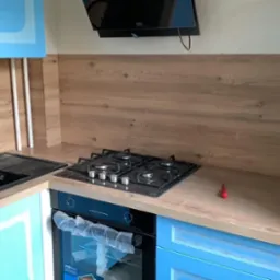 Jasna kuchnia z niebieskimi szafkami, drewnianym blatem i panelem. Czarny zlew i płyta gazowa. Nowoczesny design, po remoncie, detale wykończenia.