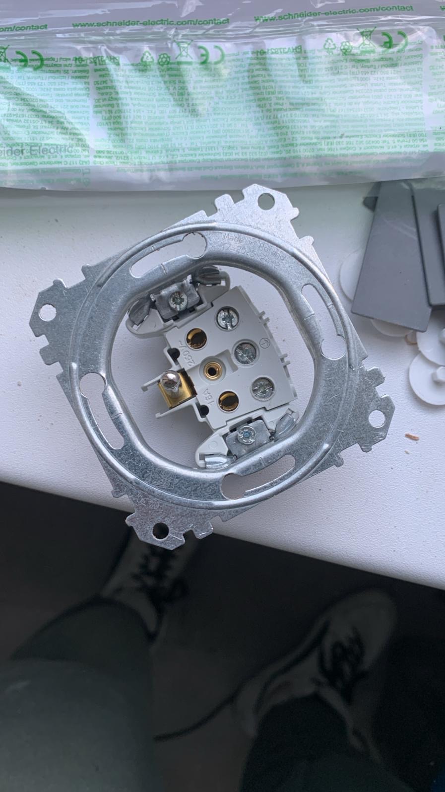 Metalowa ramka gniazdka elektrycznego Schneider Electric, widok z góry, z widocznymi elementami montażowymi i fragmentem opakowania produktu.