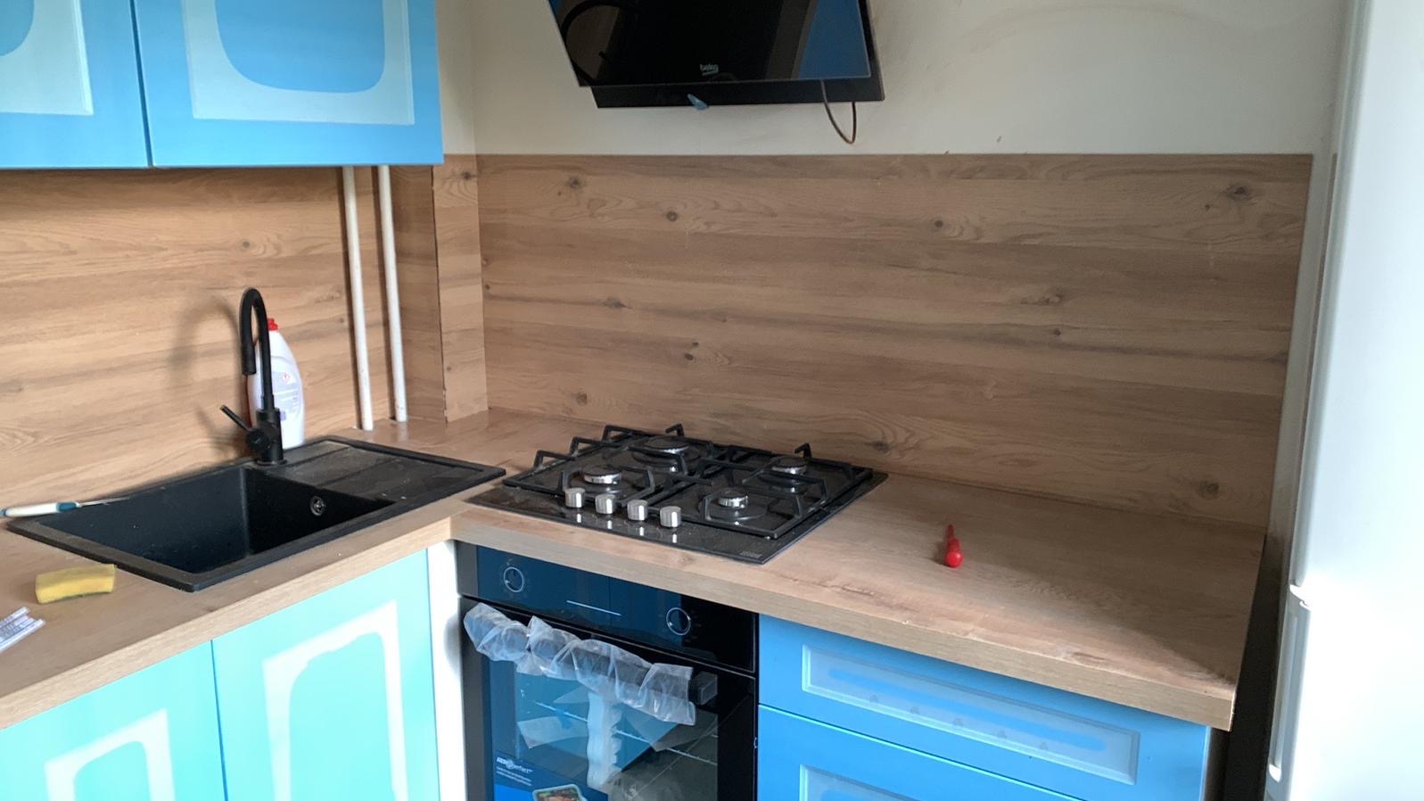 Jasna kuchnia z niebieskimi szafkami, drewnianym blatem i panelem. Czarny zlew i płyta gazowa. Nowoczesny design, po remoncie, detale wykończenia.