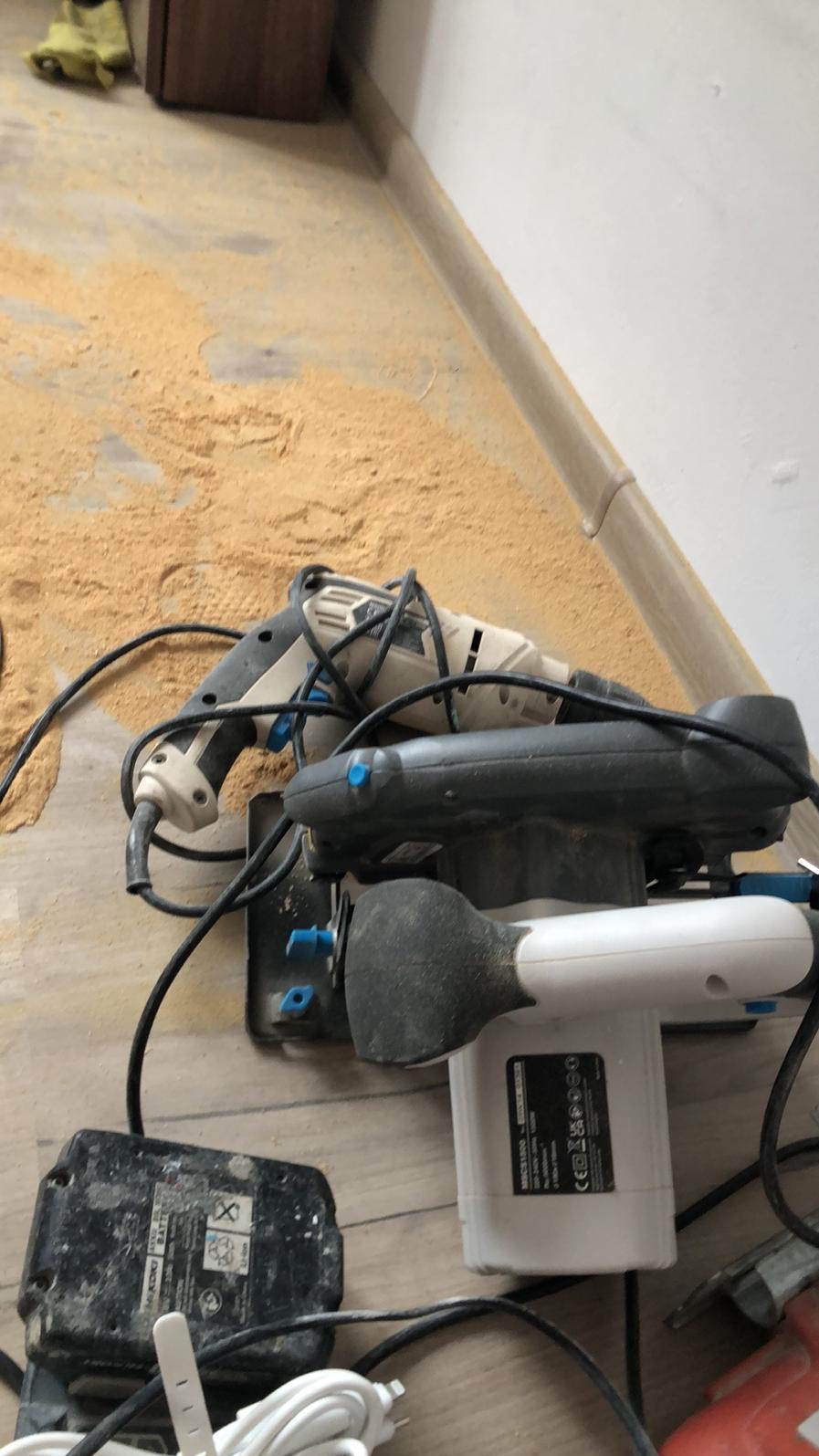 Podłoga w trakcie prac remontowych, pokryta pyłem po cięciu, z widocznymi narzędziami: szlifierką i akumulatorem. Ślady prac remontowych w pomieszczeniu.