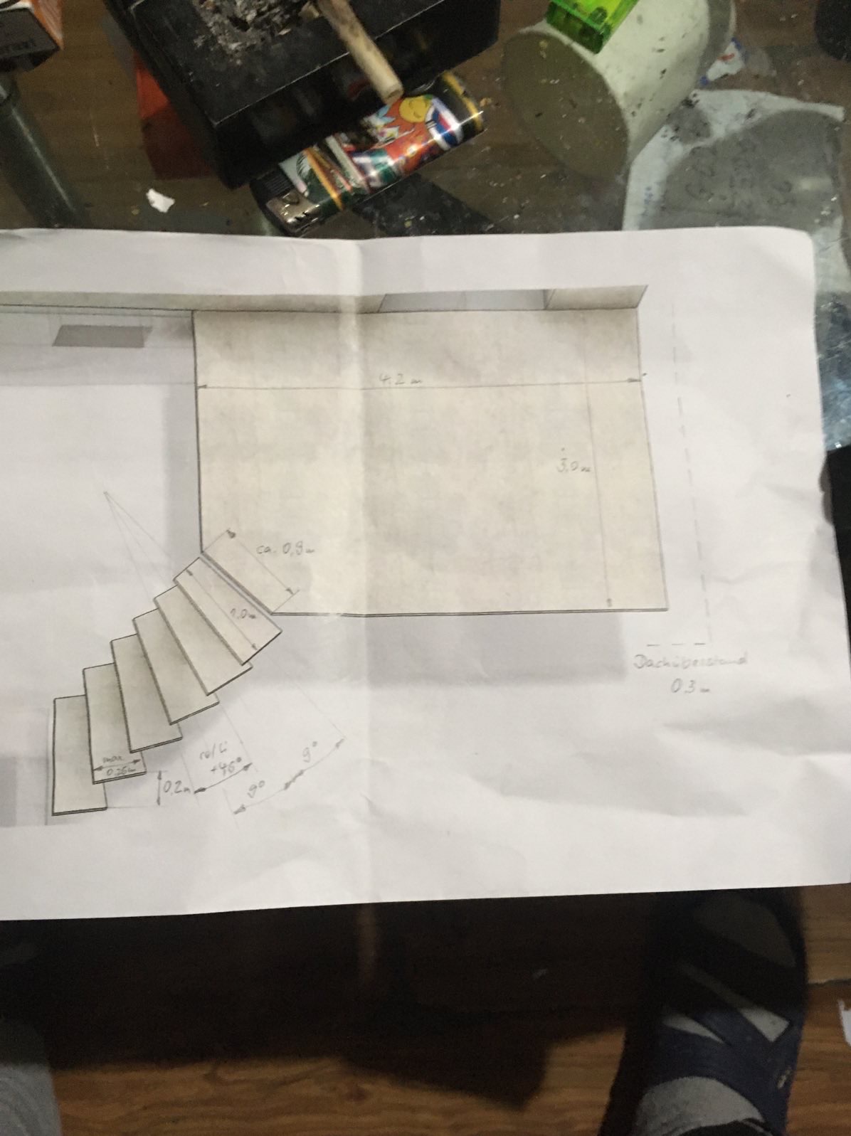 Rysunek techniczny schodów i pomieszczenia z wymiarami na białym papierze, leżący na stole z akcesoriami. Widoczne detale jak kąty nachylenia i długości.