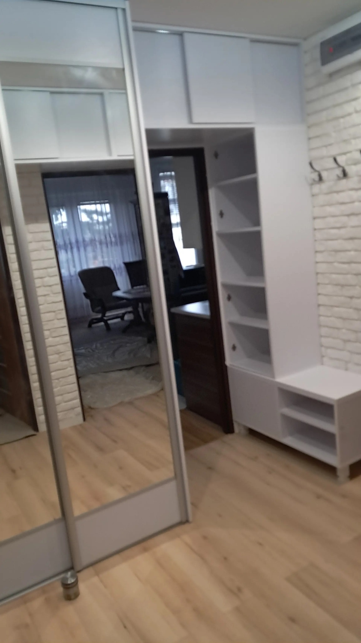 Biała szafa przesuwna z lustrem i regał z półkami w Rzeszowie. Widoczne drewniane panele podłogowe i ściana z białej cegły. Nowoczesny design.