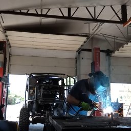 SteeLove Pomysły Art Metal Studio - Prace spawalnicze przy konstrukcji pojazdu terenowego w warsztacie w Busko-Zdroju. Widoczne iskry i spawacz w masce ochronnej, częściowo otwarte drzwi garażowe.